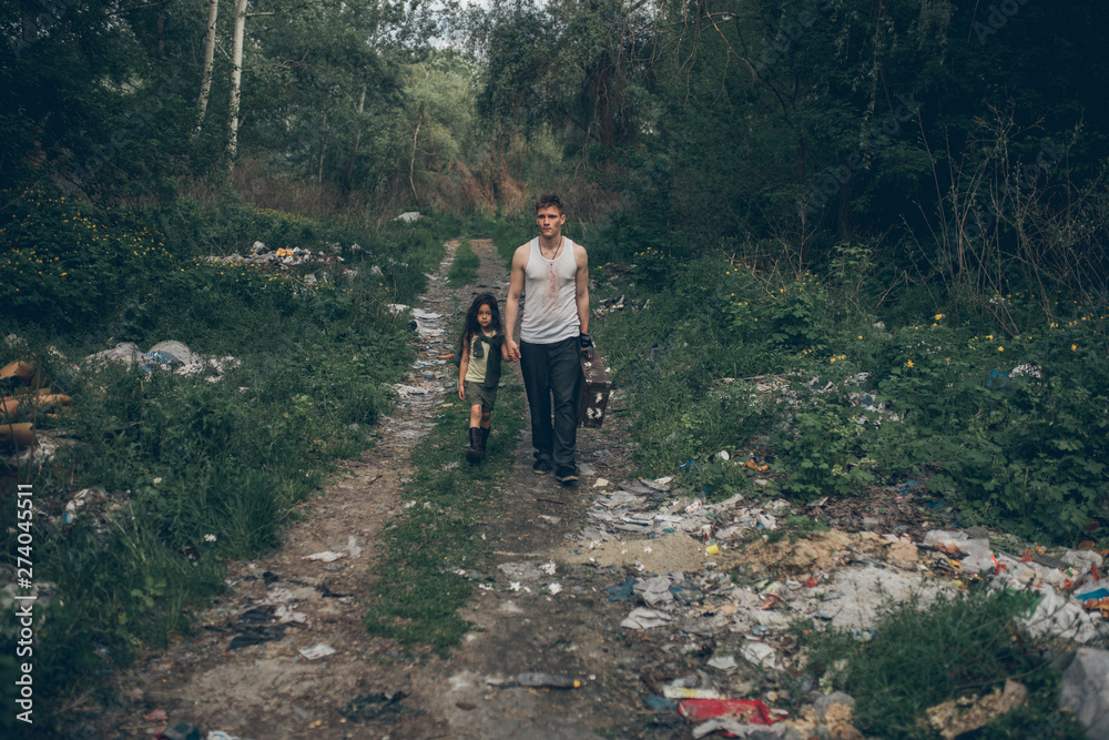 Obraz premium Homeless father and daughter walk through the garbage dump.