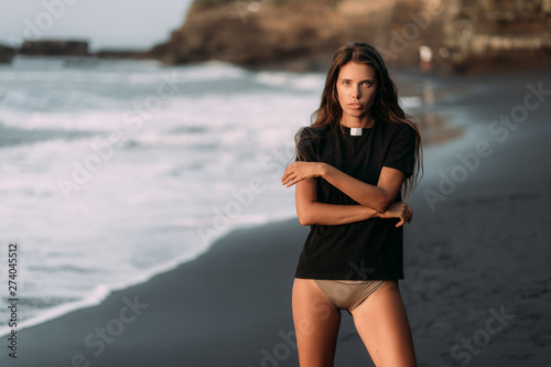 Girl in black T-shirt and swimsuit on black sandy beach in rays of sunset
