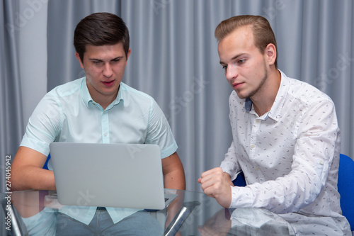 Two cheerful young businessmen working and using laptop on business meeting together