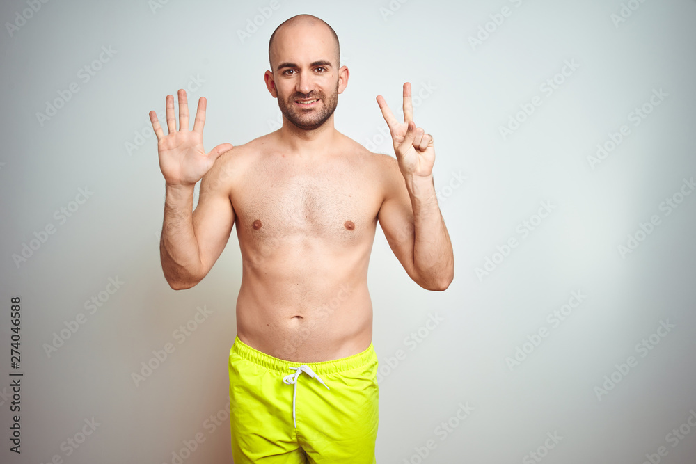Young shirtless man on vacation wearing yellow swimwear over isolated background showing and pointing up with fingers number seven while smiling confident and happy.