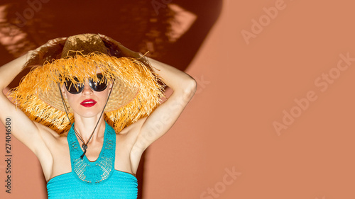Young woman wearing straw hat with fringe and swimsuit having fun over bright background, shorts, sunglasses, sunbathing, summer vacation, happiness, fun, enjoying, sunny