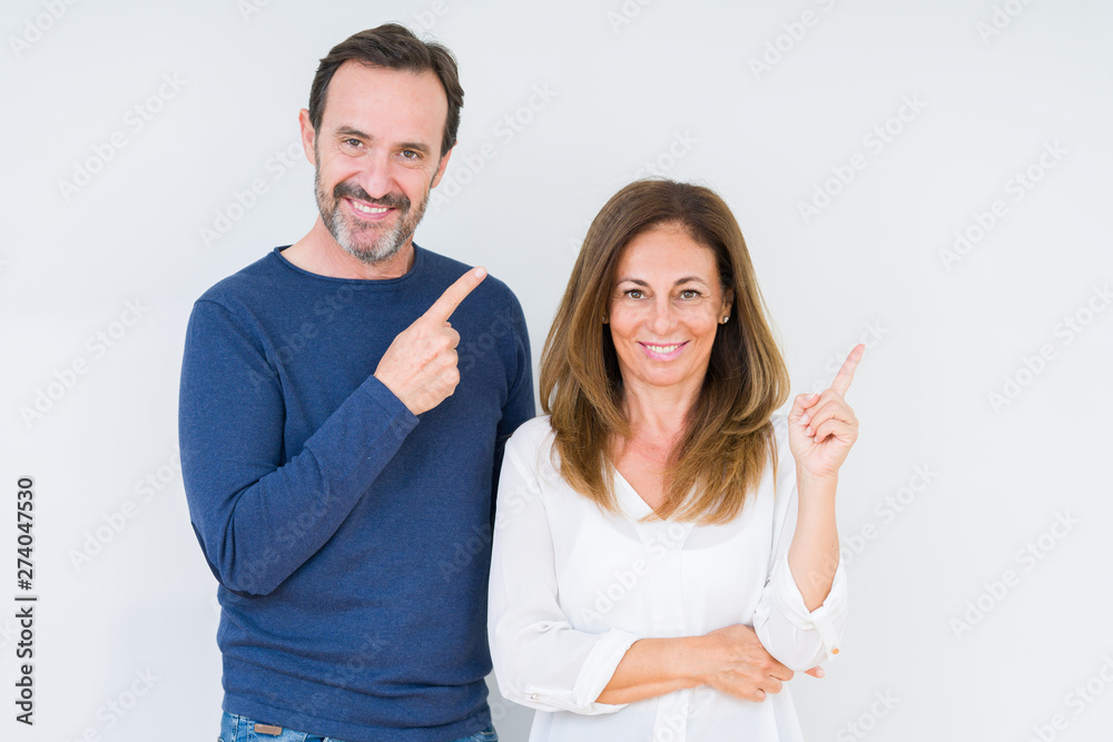 Beautiful middle age couple in love over isolated background with a big smile on face, pointing with hand and finger to the side looking at the camera. Beautiful middle age couple in love over isolated background with a big smile on face, pointing with hand and finger to the side looking at the camera.