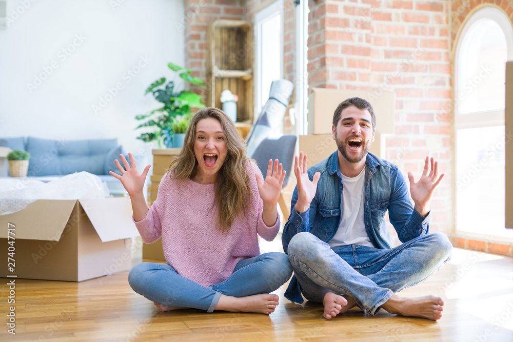 Young beautiful couple moving to a new house sitting on the floor celebrating crazy and amazed for success with arms raised and open eyes screaming excited. Winner concept Young beautiful couple moving to a new house sitting on the floor celebrating crazy and amazed for success with arms raised and open eyes screaming excited. Winner concept