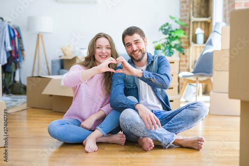 Young beautiful couple moving to a new house sitting on the floor smiling in love showing heart symbol and shape with hands. Romantic concept. © Krakenimages.com