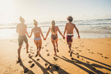 Group of young people friends enjoying with fun the summer holiday vacation running at the beach to the water in playful outdoor leisure activity together - youthful men and women