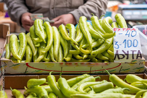 Pile of green peppers on the stand ready for sale on the marketplace in Belgrade. Blurred background of seller counting money. Letters 