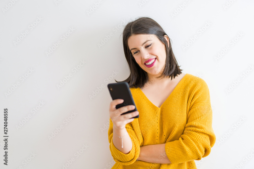 Beautiful brunette young woman smiling confident using smartphone over isolated white background wearing casual yellow sweater Beautiful brunette young woman smiling confident using smartphone over isolated white background wearing casual yellow sweater