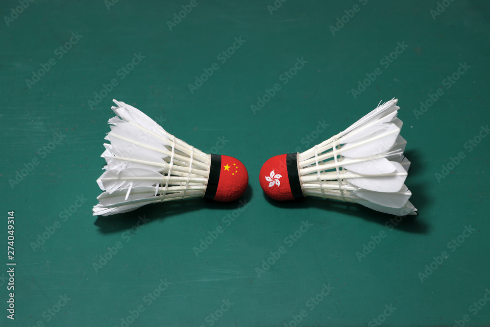 Two used shuttlecocks on green floor of Badminton court with both head each other. One head painted with China flag and one head painted with the Hong Kong flag. Two used shuttlecocks on green floor of Badminton court with both head each other. One head painted with China flag and one head painted with the Hong Kong flag.