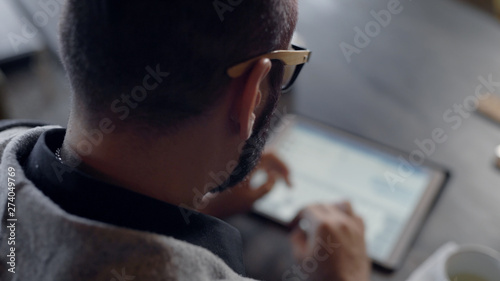 adult man is working with tablet using wireless internet, browsing sites and typing on touch screen