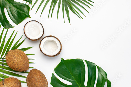 Tropical leaves and fresh coconut on light gray background. Flat lay, top view, copy space. Summer background, nature. Healthy cooking. Creative healthy food concept, half of coconut