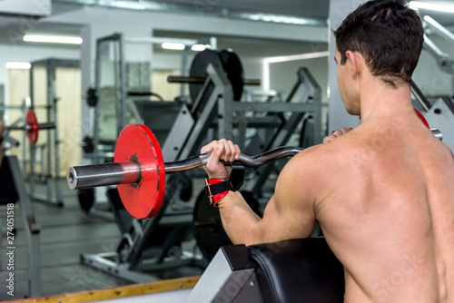 Athlete man lifting dumbbell in gym, back view