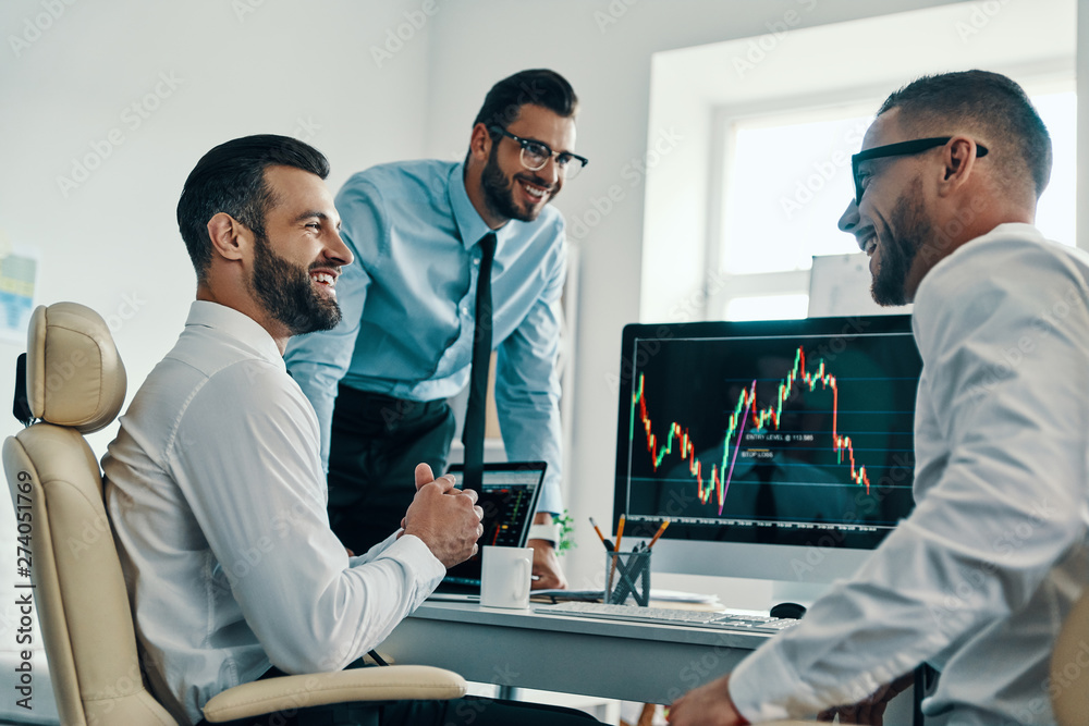 Obraz premium Successful traders. Group of young modern men in formalwear analyzing stock market data while working in the office