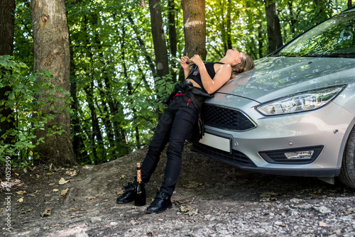 Drunk woman standing near car with bottle