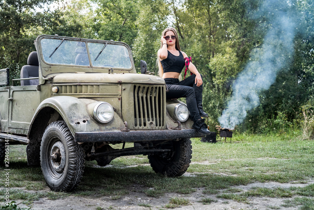 Fototapeta premium Woman outdoors sitting on hood of military car