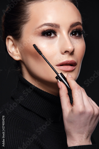 Beauty Cosmetics.Woman applying black mascara on eyelashes with makeup brush. photos of appealing brunette girl on black background.High Resolution