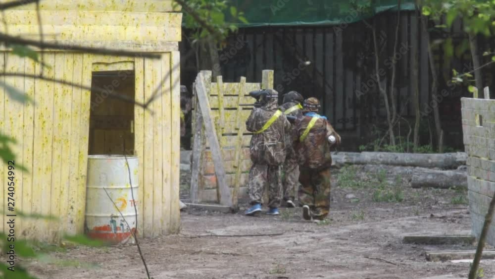 Children and teenagers play paintball. Several players are hiding behind cover. One of the players leaves the battlefield. Children and teenagers play paintball. Several players are hiding behind cover. One of the players leaves the battlefield.