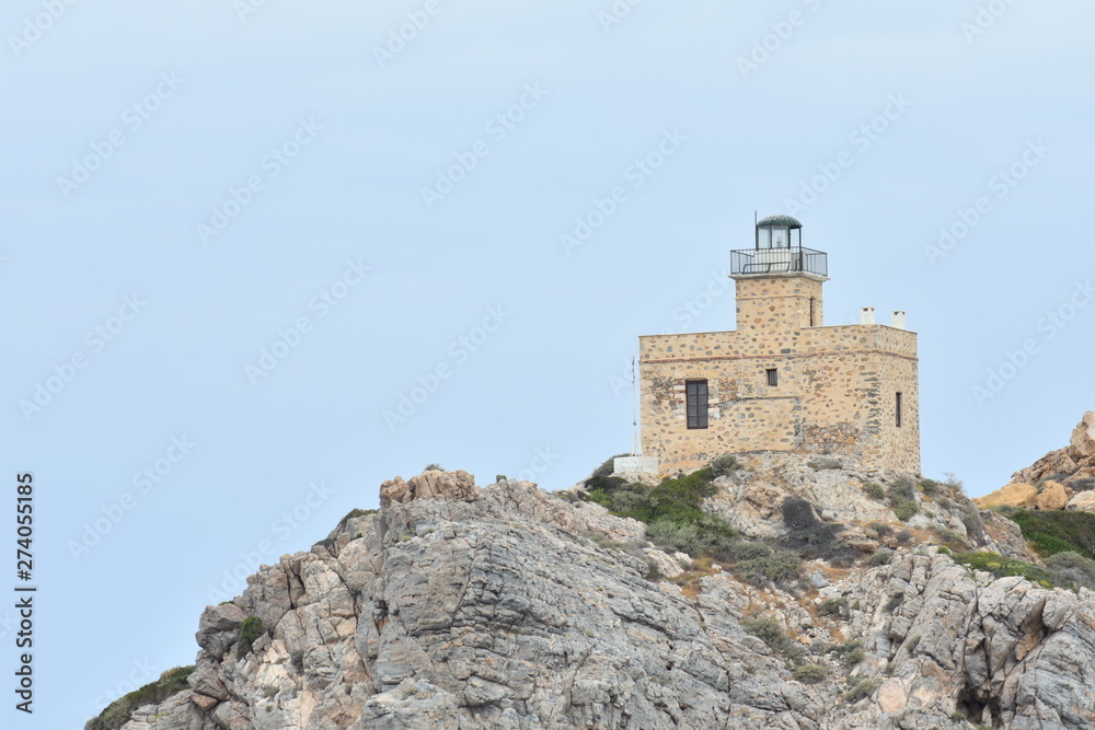 The holiday island of Ios in Greece. As the ferry sails into the sheltered bay a lighthouse stands sentinel above jagged rocks at the ports entrance.