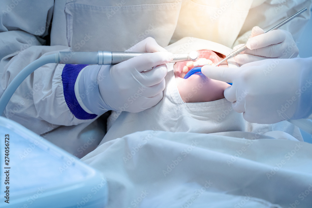 Fototapeta premium Female dentist using instrument for curing and drilling patient teeth in dental clinic. Dental procedure and medical treatment.