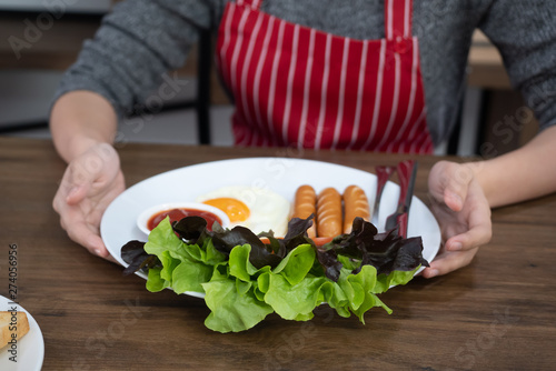Woman hands holding american breakfast, sausage, fried egg and fresh vegetable healthy salad on white plate for new day.