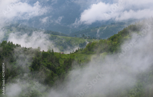 Cloudy Rural Mountain Landscape With Summer Morning Fog In Matisesti Area Of Apuseni National Park,Romania. Beautiful Countryside Landscape With Forested Hills, Old House And White Clouds,Transylvania