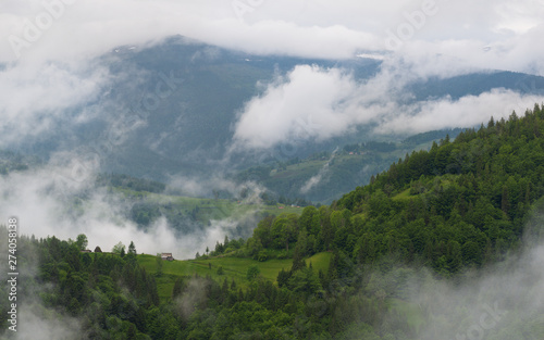 Countrified Summer Foggy Landscape Of Apuseni National Park In Romania. Rural House On A Green Forest Slope Among The Romanian Mountains, Transylvania.Countryside Summer Scenery. House In The Clouds