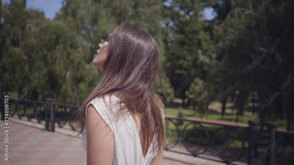 Portrait glamorous young girl wearing sunglasses and a long white summer fashion dress walking outdoors. Leisure of a pretty woman in the park. Slow motion. Portrait glamorous young girl wearing sunglasses and a long white summer fashion dress walking outdoors. Leisure of a pretty woman in the park. Slow motion.