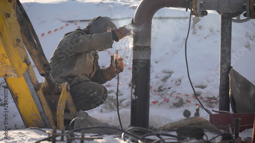 Worker produces pipe welding on the street. In winter, at low temperatures, it is difficult to mount the pipe wire.