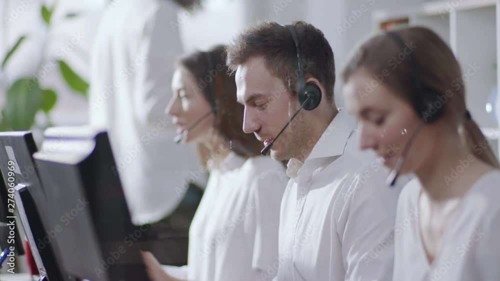Business and technology concept - helpline operator with headphones in call centre working hard, then looks straight to camera and smiles happily. Politeness, good mood, positive emotions. Female Business and technology concept - helpline operator with headphones in call centre working hard, then looks straight to camera and smiles happily. Politeness, good mood, positive emotions. Female