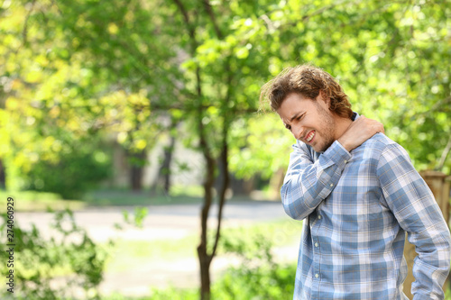 Young man suffering from pain in shoulder outdoors