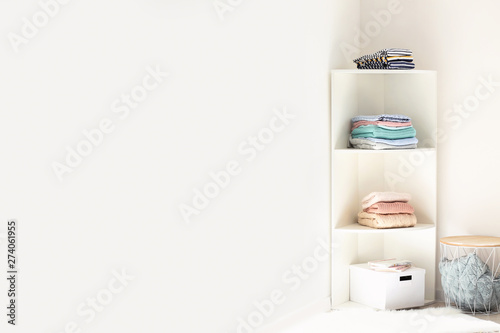 Rack with stacks of clean clothes near white wall