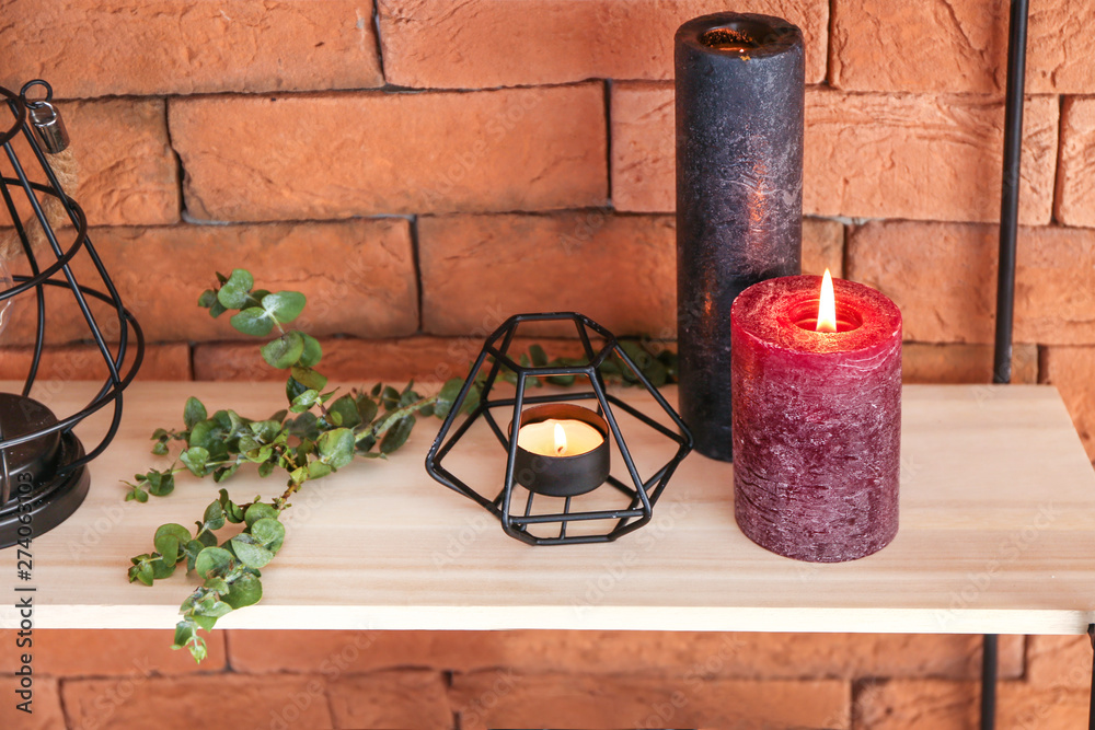 Burning candles and eucalyptus branches on shelf near color wall
