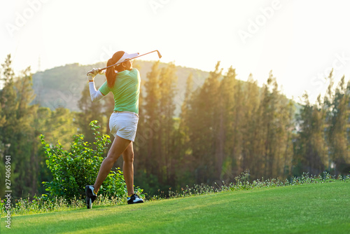 Healthy Sport. Asian Sporty woman golfer player doing golf swing tee off on the green evening time, she presumably does exercise. Healthy Lifestyle Concept.