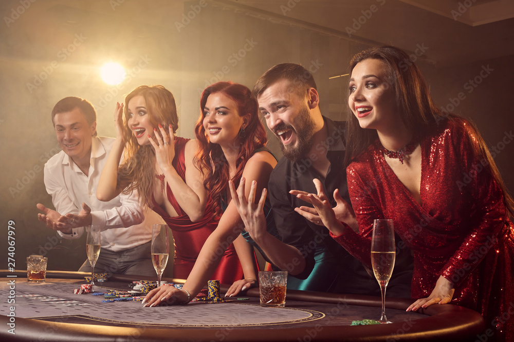 Group of a young rich friends are playing poker in casino. - obrazy, fototapety, plakaty 