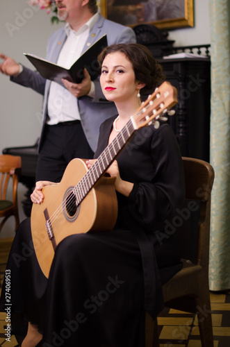 Beautiful girl performs playing acoustic guitar in a black dress