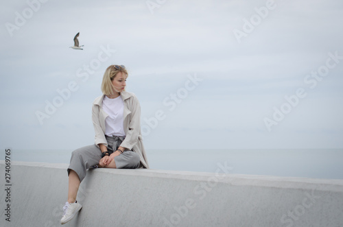 Young attractive girl sitting gray concrete wall against the gray sky