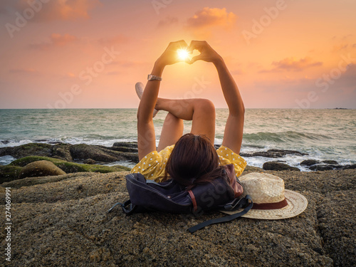 Hipster woman lying on the rock show the hand of heart in sunset time.