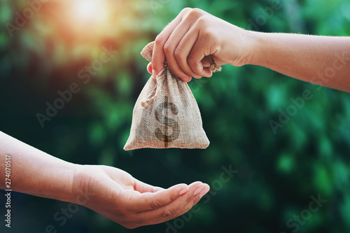 hand giving money bag to another people on green background with sunrise