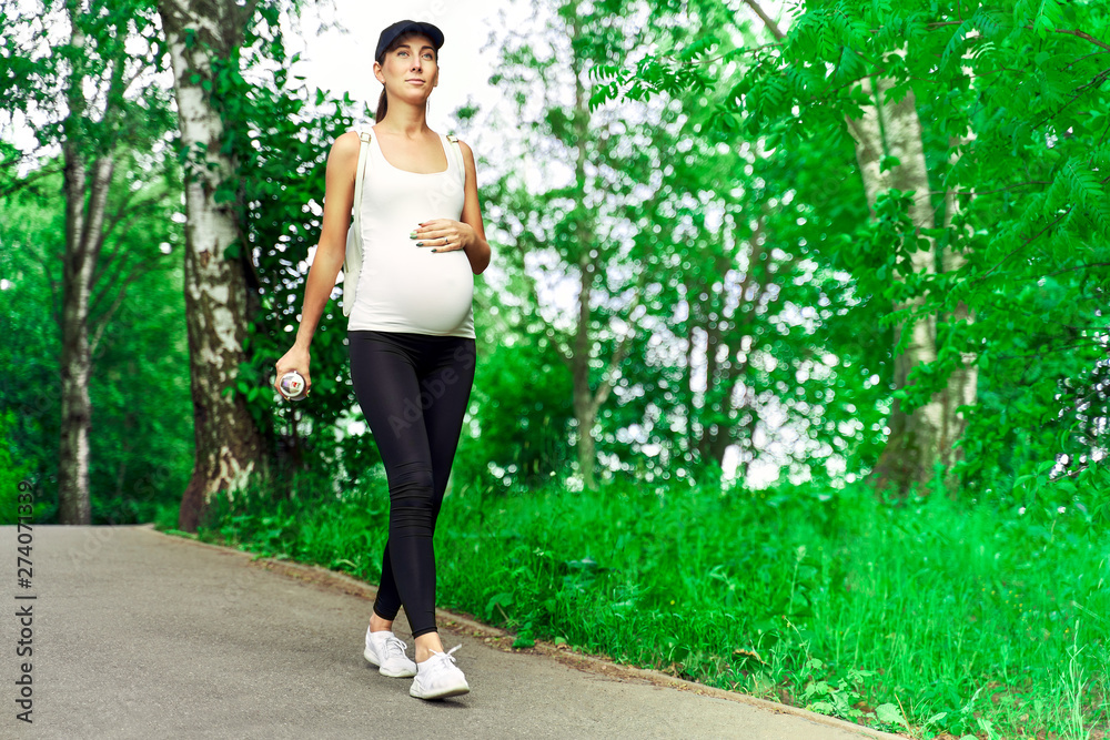 Sports modern young woman in late pregnancy walks in sportswear in a green summer Park among the birches. The concept of unity with nature and sports walking Sports modern young woman in late pregnancy walks in sportswear in a green summer Park among the birches. The concept of unity with nature and sports walking
