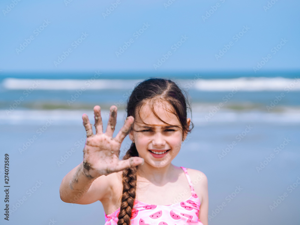 Summer beach. Little girl have a good time of resort beach. Teen girl playing on sandy beach. Focus on the hand . Close-up view. Summer travel and vacation concept