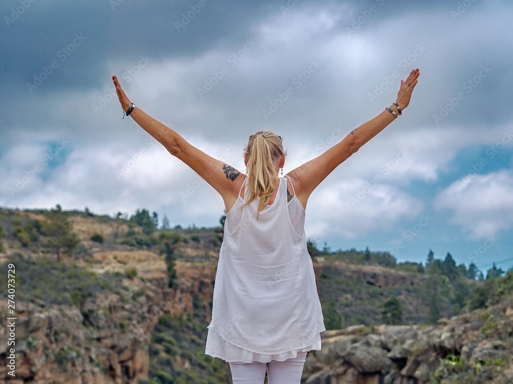 A woman in white summer clothes stands with her back to the photographer, arms outstretched A woman in white summer clothes stands with her back to the photographer, arms outstretched