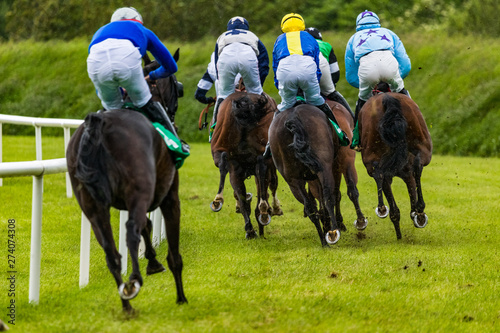 Close up on galloping race horses and jockeys in the rain, view from behind