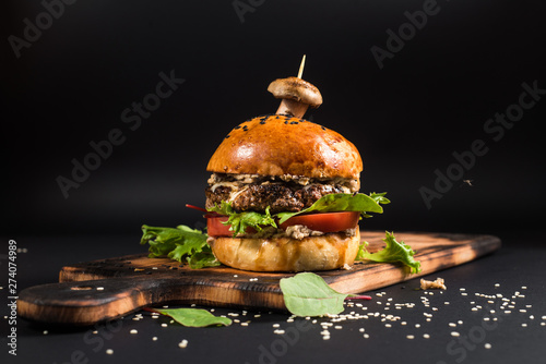 Tasty burger with grilled meat and mushroom on the black background