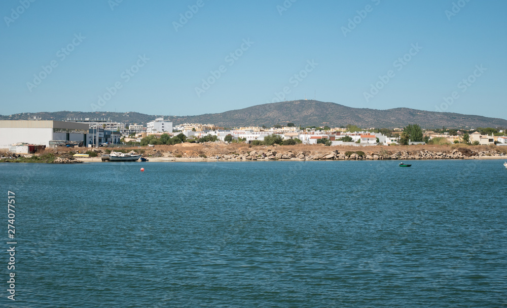 View from ocean to shore in Algarve, Portugal in summer with boat on beach, houses and hills in background.