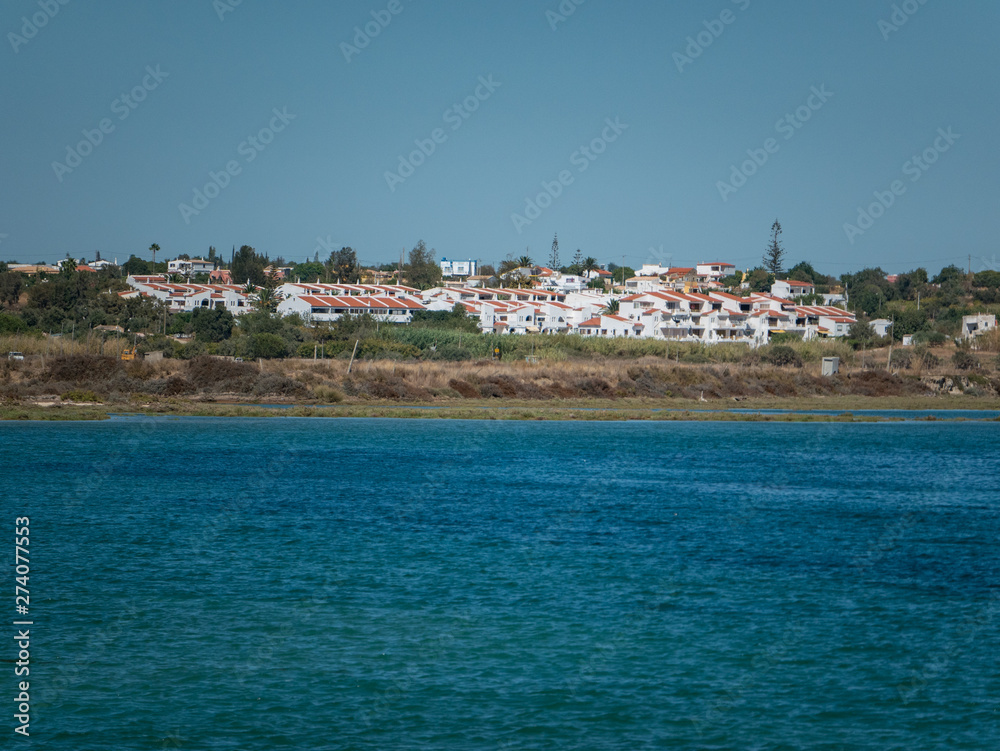 Wide shot of coast of Algarve, Portugal on sunny summer day with houses and trees. Shot from boat with ocean in foreground.