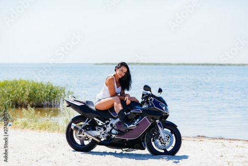 Young amazing sexy woman posing near motorbike on the beach, wearing stylish crop top , shirts, have perfect fit slim tamed body and long hairs. Outdoor lifestyle portrait.