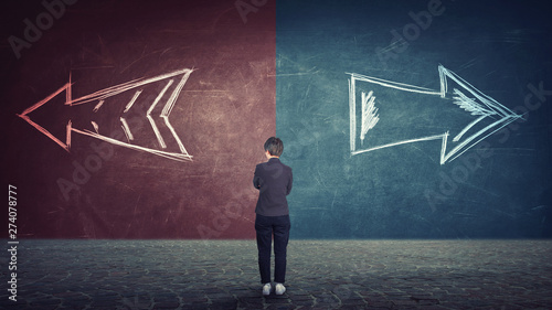 doubtful businesswoman in front of a split wall as arrows leads in two different ways red and blue side. Correct choice left or right, failure or success photo