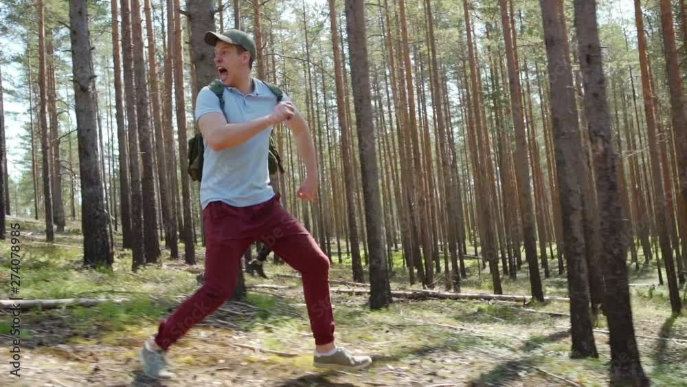 Tracking right shot of two awfully scared young men with backpacks running through forest in slow motion fleeing from danger and screaming awfully terribly