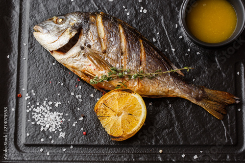 Delicious grilled dorado or sea bream fish with lemon slices, spices, rosemary on dark stone. Grilled sea fish with olive oil, spices and lemon ready for eating. Dorado, herbs and spices. Menu photo photo