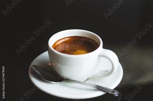 close up modern hot black coffee the espresso on dark background with coffee bubble foam pattern and texture in white cup looking and feel so delicious on glasses table in coffee shop.