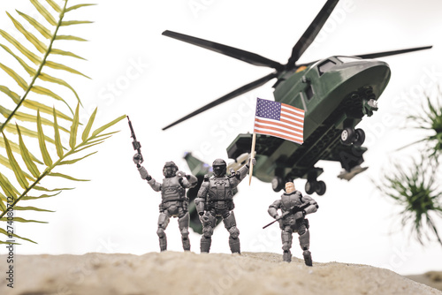 plastic toy soldiers on sand dune with guns and american flag near copter in sky